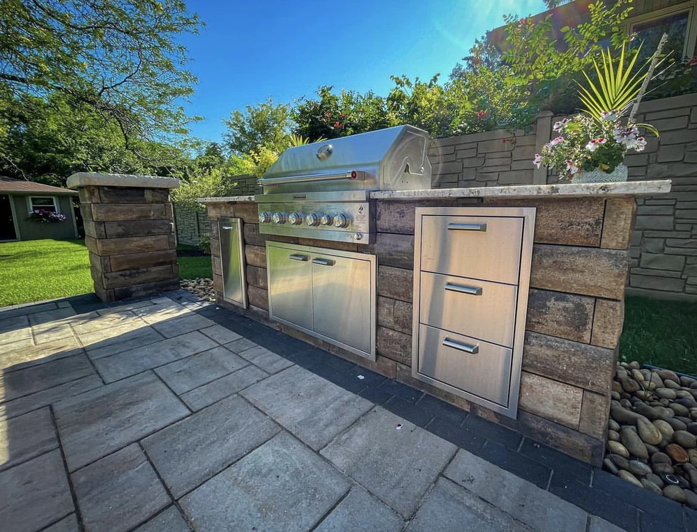 Curbscapes Outdoors hardscaping huntertown in - Curbscapes Outdoors Outdoor kitchen with stainless grill. storage drawers. stone counters. and a paver patio in a sunny yard.