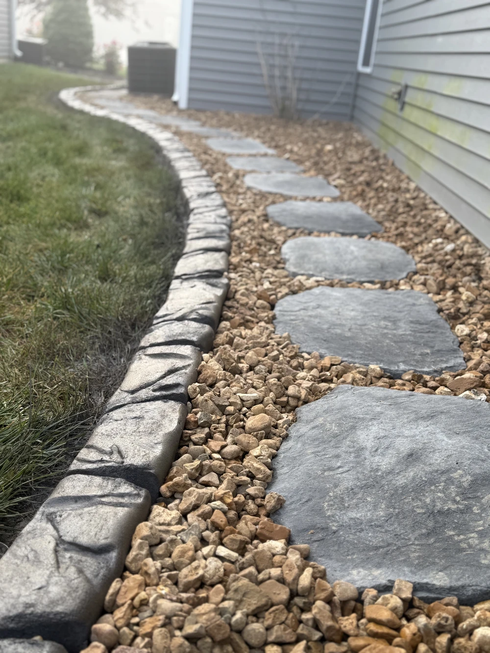 Curbscapes Outdoors landscaping fort wayne in - Curbscapes Outdoors Concrete curbing lines a side yard path with gravel and large stepping stones beside the house.