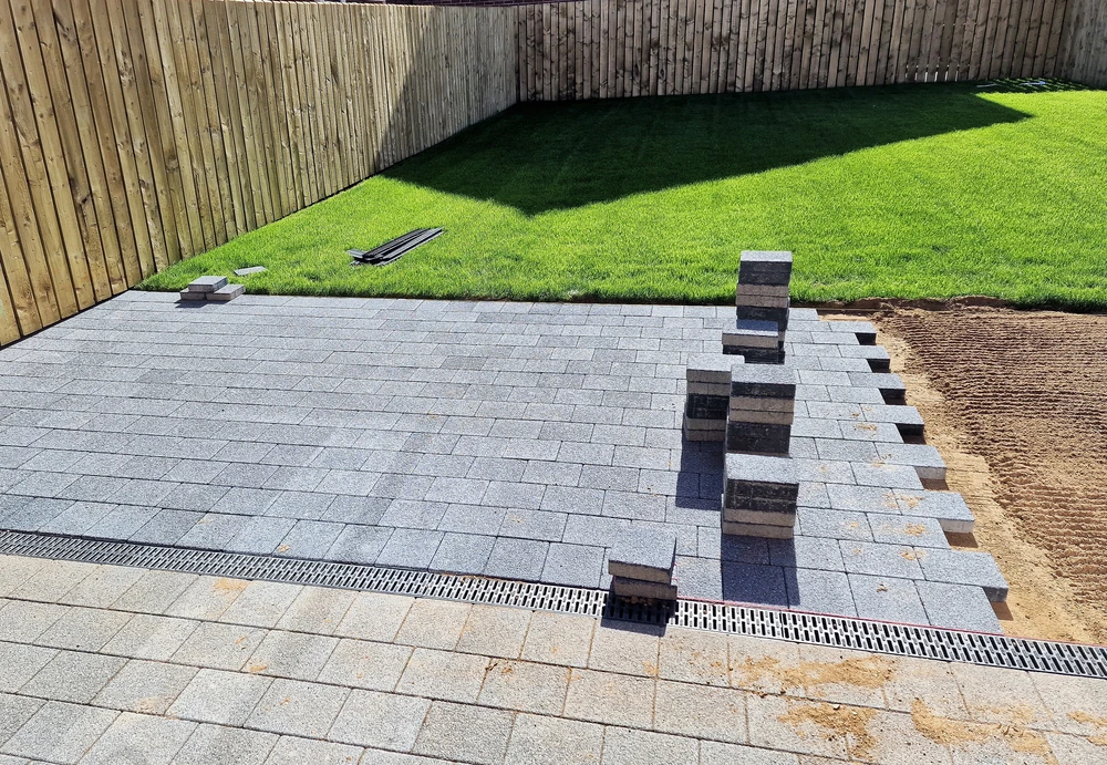 Curbscapes Outdoors masonry auburn in 3 - Curbscapes Outdoors New backyard pavers patio with linear drain installed beside a wood fence and bright green lawn.