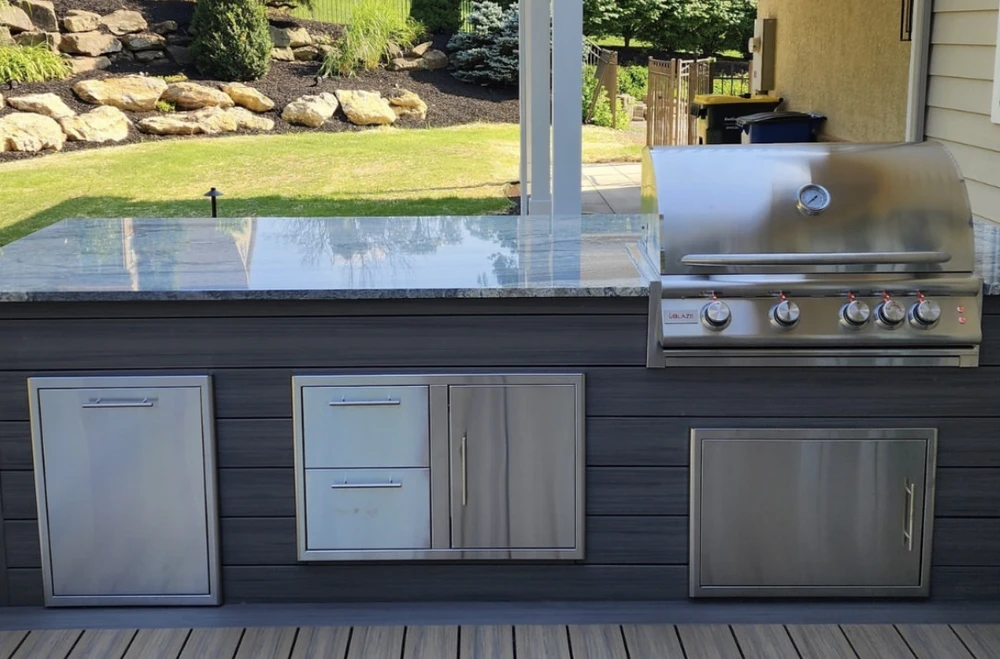 Curbscapes Outdoors outdoor kitchen huntertown in - Curbscapes Outdoors Outdoor kitchen with stainless grill. built-in storage. polished stone counter. and grassy backyard view.