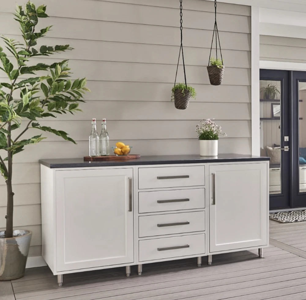 Curbscapes Outdoors outdoor living spaces fort wayne in - Curbscapes Outdoors Covered patio cabinet setup for an outdoor kitchen with white storage. black counter. plants. and hanging baskets.