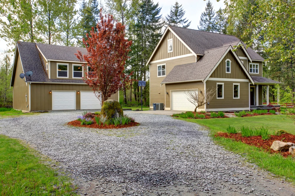 Curbscapes Outdoors landscaping auburn in - Curbscapes Outdoors Gravel driveway landscaping with garden beds. Red mulch. Trees. Large rock accents around a beige home.