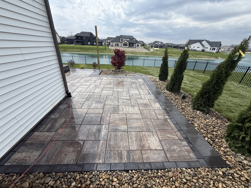 curbscapefw service area 3 - Curbscapes Outdoors Gray and tan paver hardscaping fills the side patio. Dark edging and river rock frame tall evergreens beside a pond.