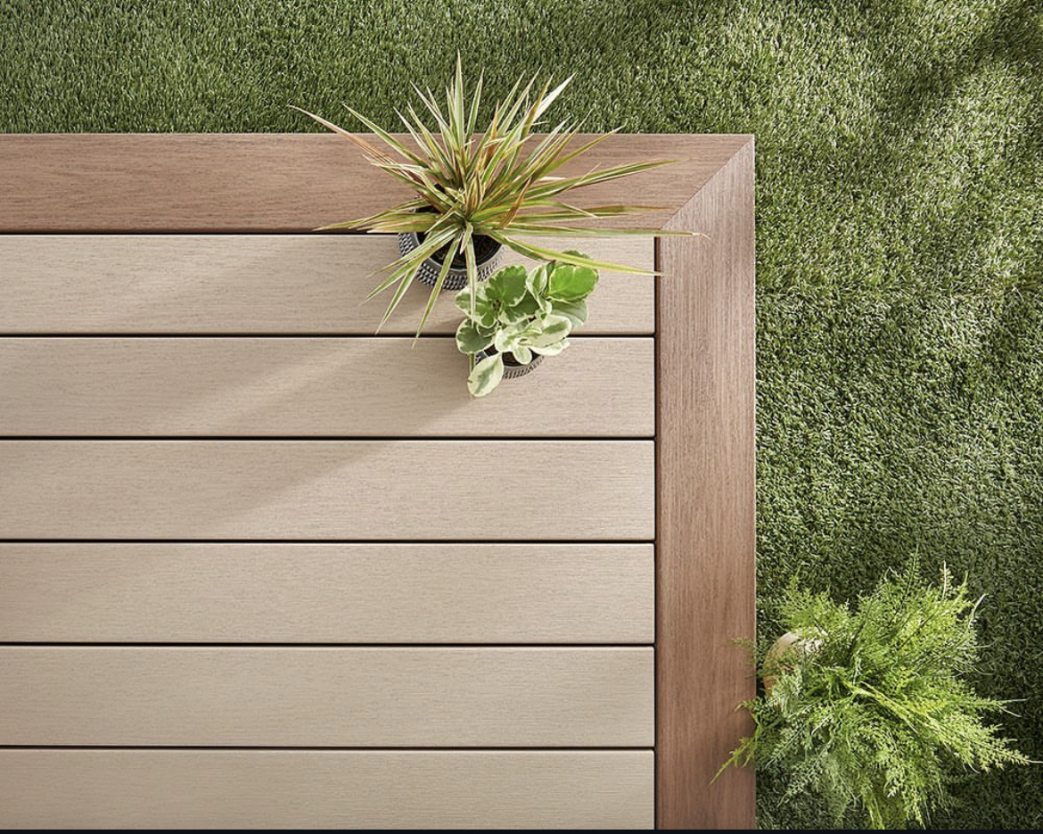 curbscapes blog week1 2 - Curbscapes Outdoors Brown composite deck boards form a crisp framed corner beside dense green turf. Two small potted plants rest along the upper inner edge.