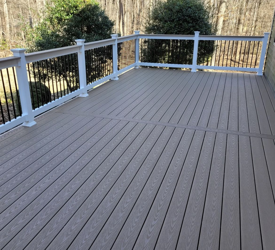 curbscapes blog week1 3 - Curbscapes Outdoors Wide gray deck boards span an empty platform enclosed by white posts and black balusters. Rounded shrubs and bare woods stand beyond the railing.